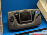 Black Sega Game Gear handheld displayed upright on a Retro Craft 3D printed stand, on a blue shelf beside a Sega Saturn box