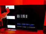 MiSTer Laggy sensor held against an OLED TV running the MiSTerLaggy core, showing on-screen display-latency readings in milliseconds