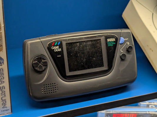 Black Sega Game Gear handheld standing upright on display against a blue background, beside a Sega Saturn game box