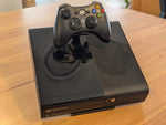 Xbox 360 E console on its display stand, with a controller held in the built-in holder