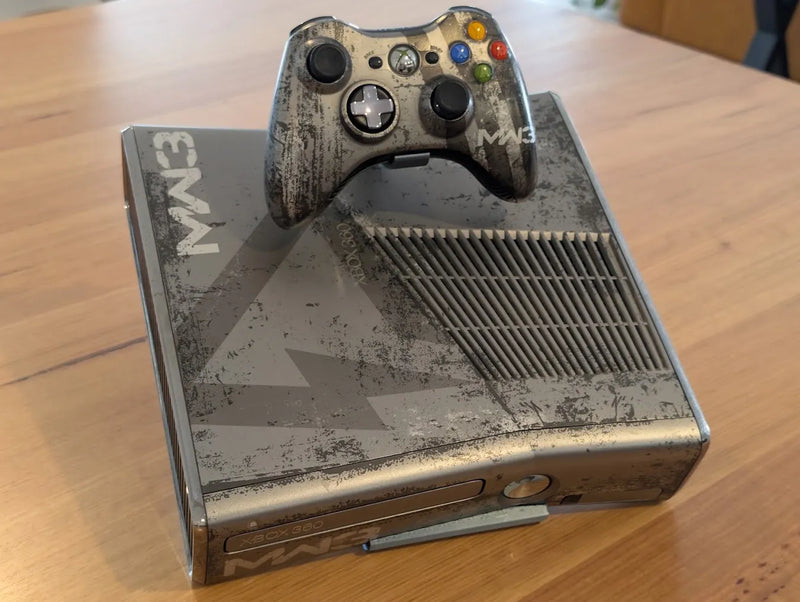 Xbox 360 S console on its display stand, with a controller held in the built-in holder